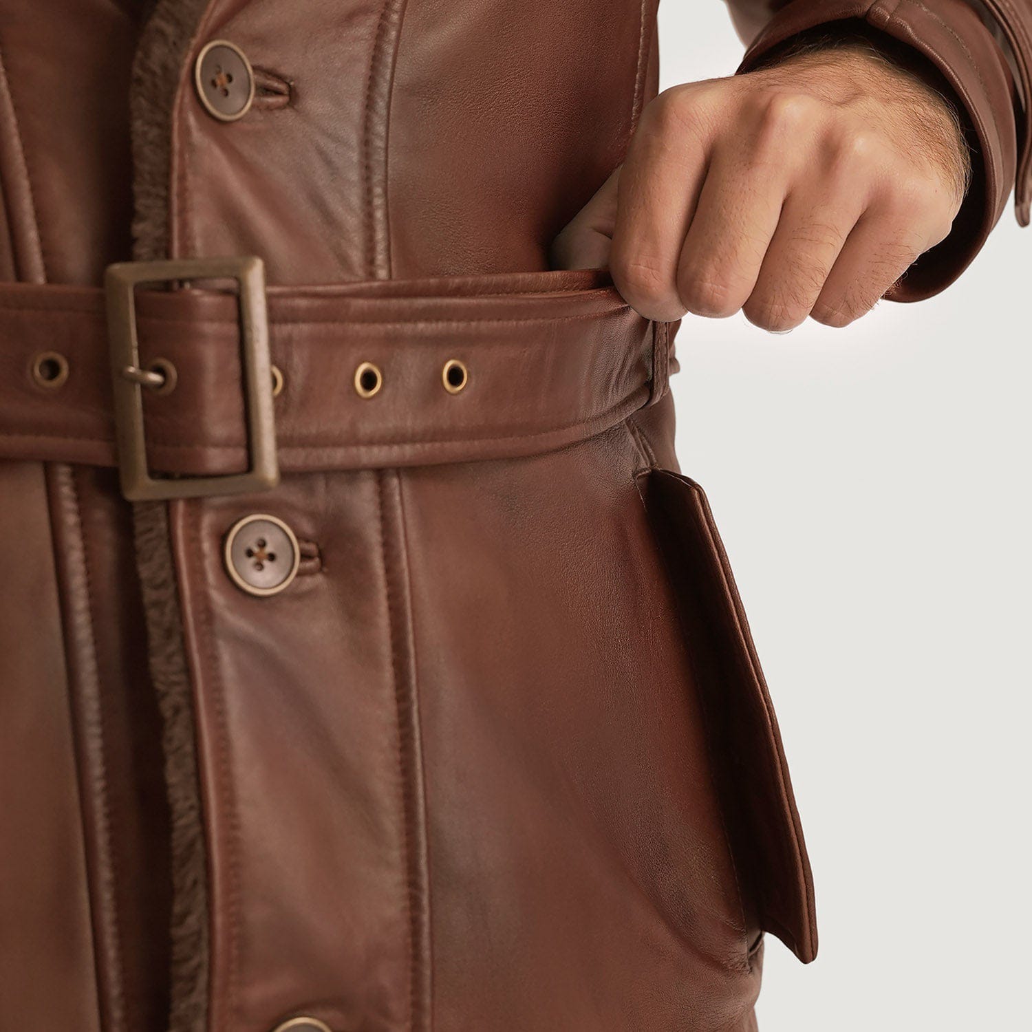 Close-up of a brown leather trench coat with a belt and buttons on a light gray background